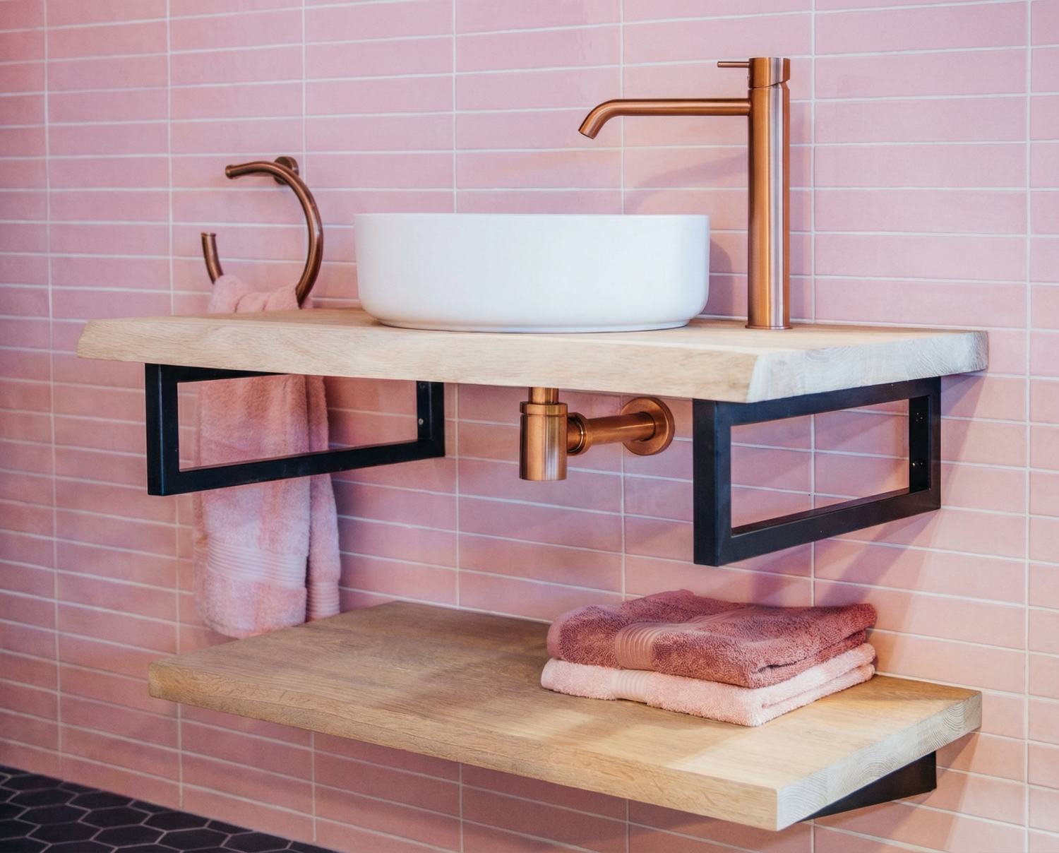 Roze tegelwand in de badkamer met witte opbouwwastafel, houten planchet en koperkleurige kraan