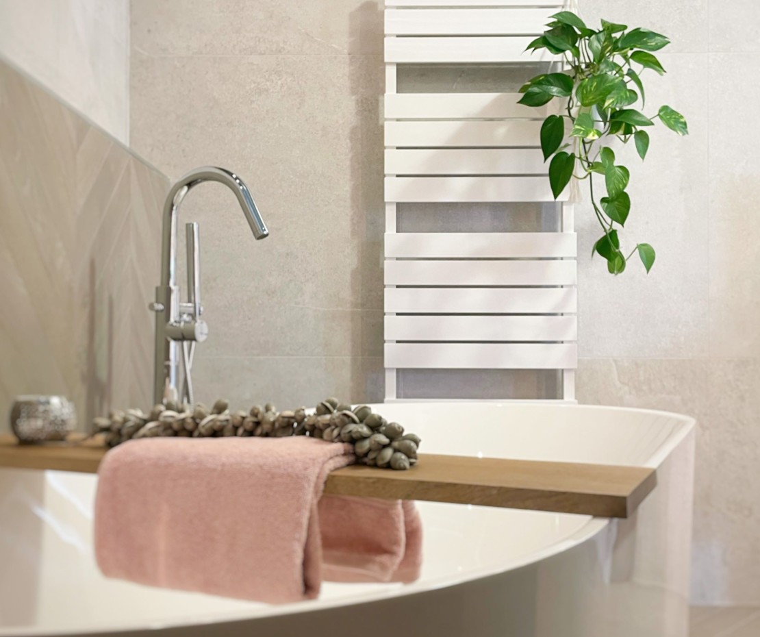 Vrijstaand bad met houten plank, roze handdoek en witte designradiator op lichtgrijze tegelwand